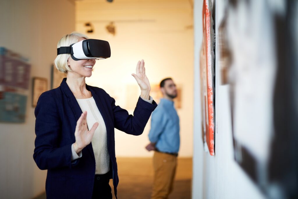 Eine Frau mit VR-Headset erlebt eine virtuelle Ausstellung, während ein Mann im Hintergrund traditionelle Kunstwerke betrachtet