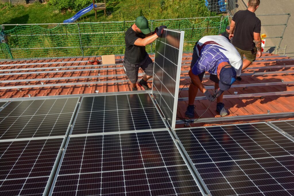 Handwerker montieren eine Photovoltaikanlage auf einem Dach, was die Bedeutung der Frage hervorhebt, wer Photovoltaik installieren darf, um eine sichere und effiziente Installation zu gewährleisten.