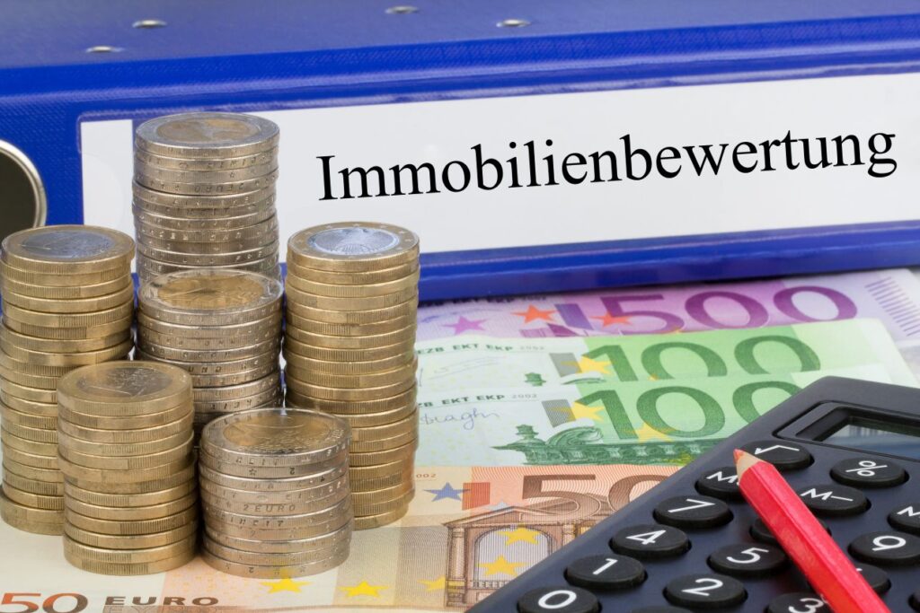 Geldmünzen, Euro-Banknoten und Taschenrechner vor Ordner mit Aufschrift Immobilienbewertung Reutlingen – Symbolbild für Immobilienwert-Berechnung