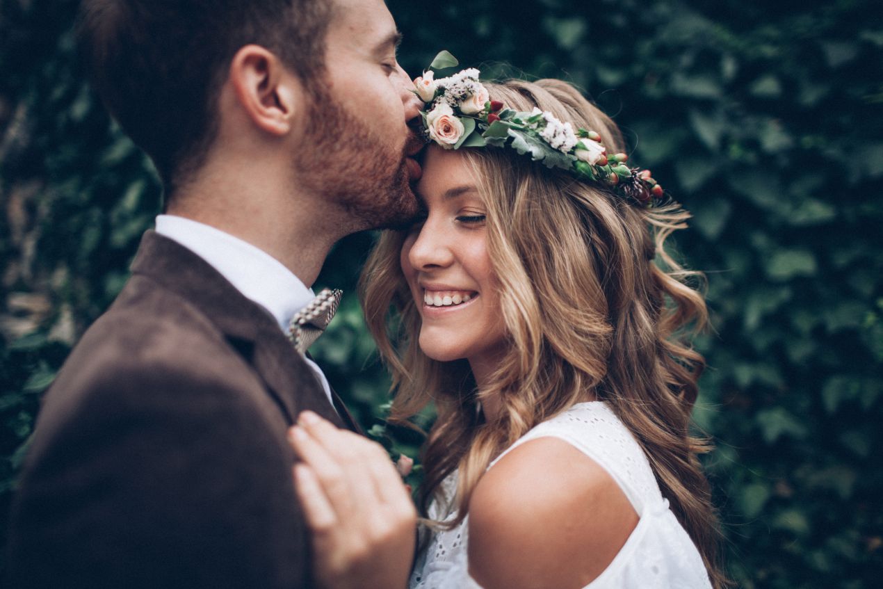 Laechelndes Paar in Hochzeitskleidung, inspiriert von Boho-Stil, traegt Eheringe aus dem Trauring Konfiguator