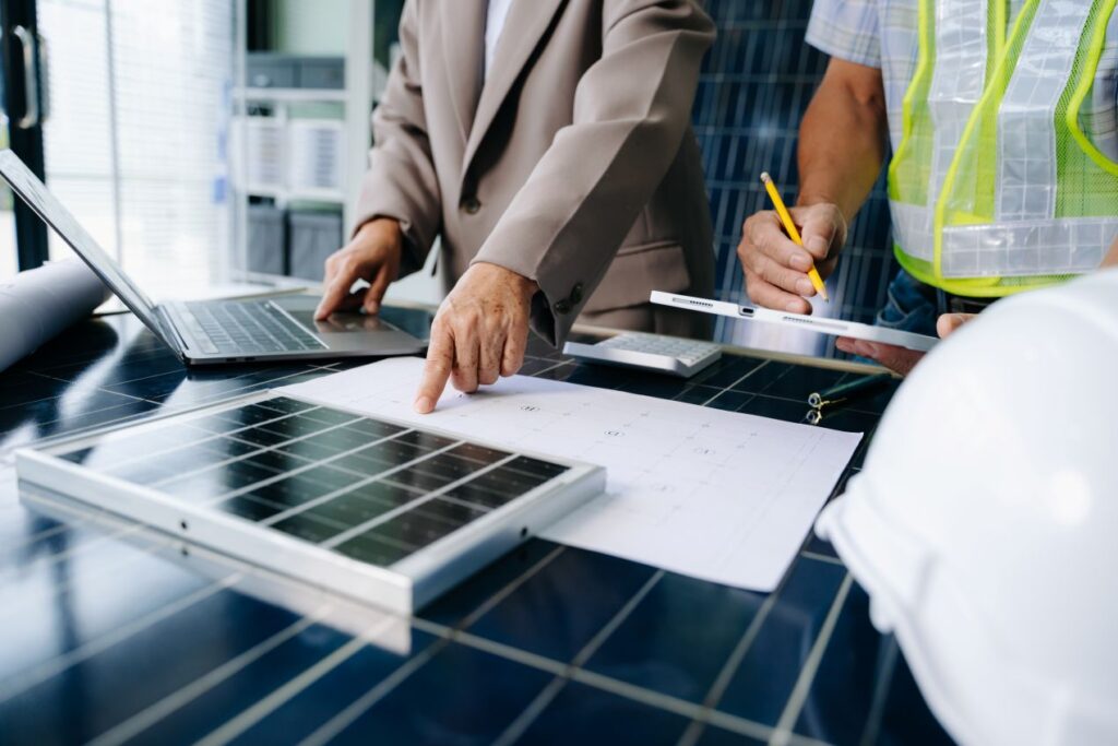 Fachleute planen ein SMA Hybrid PV-System mit Solarmodul, Laptop und Bauplaenen am Tisch
