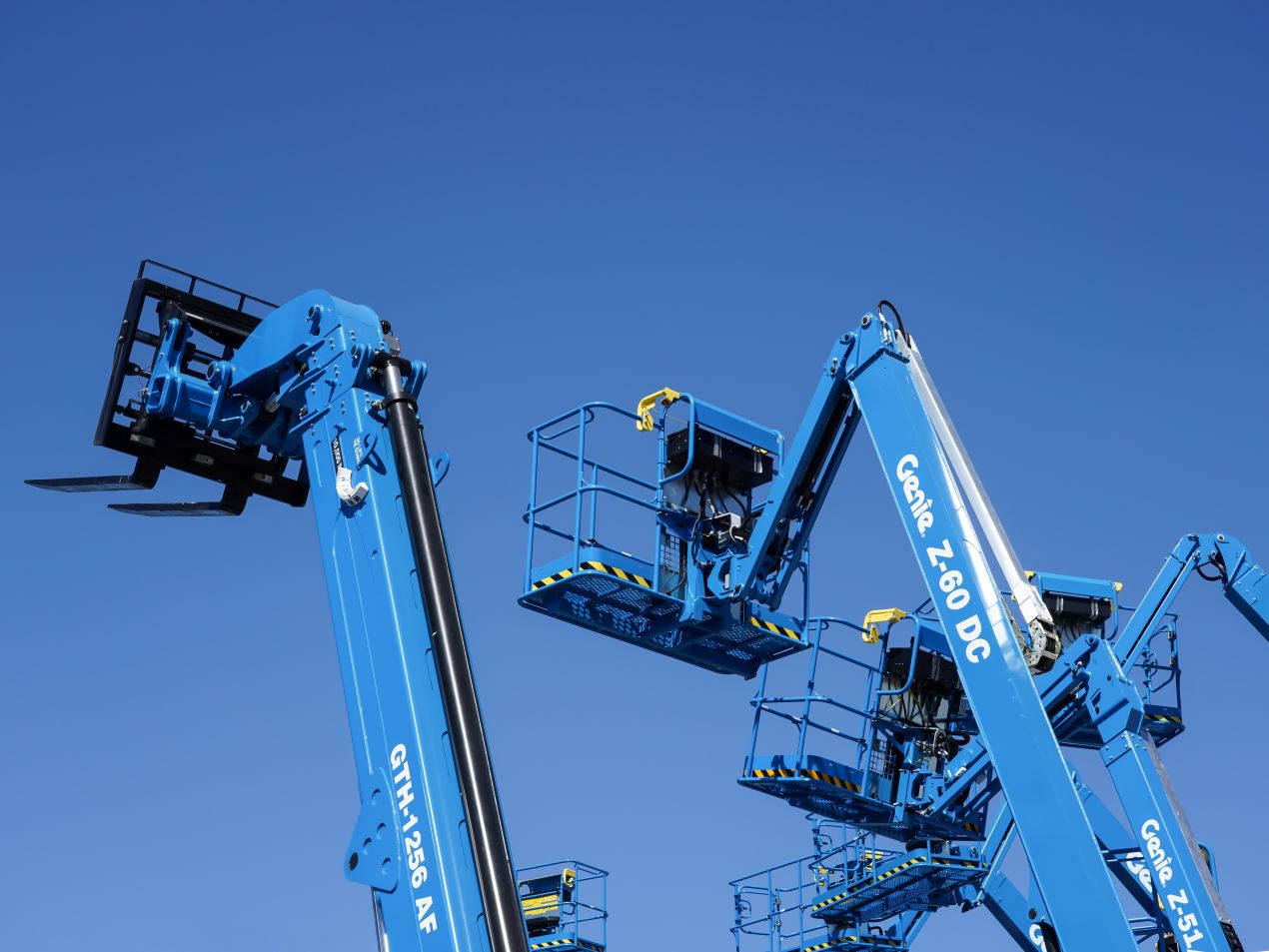 Blaue Hubarbeitsbühnen mit Arbeitskörben vor blauem Himmel, Symbolfoto für Schulung Hubarbeitsbühnen und praxisnahe Sicherheitsunterweisung